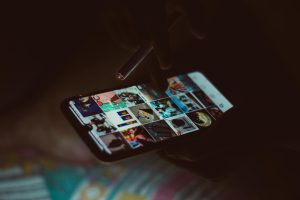 Close-up of a hand holding a smartphone and cigarette, browsing images.